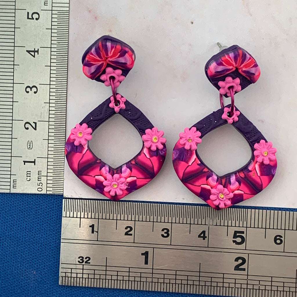 Award-winning Rennique hand-sculpted red diamond shape fashion earrings with pink floral accents shown with ruler size guide.