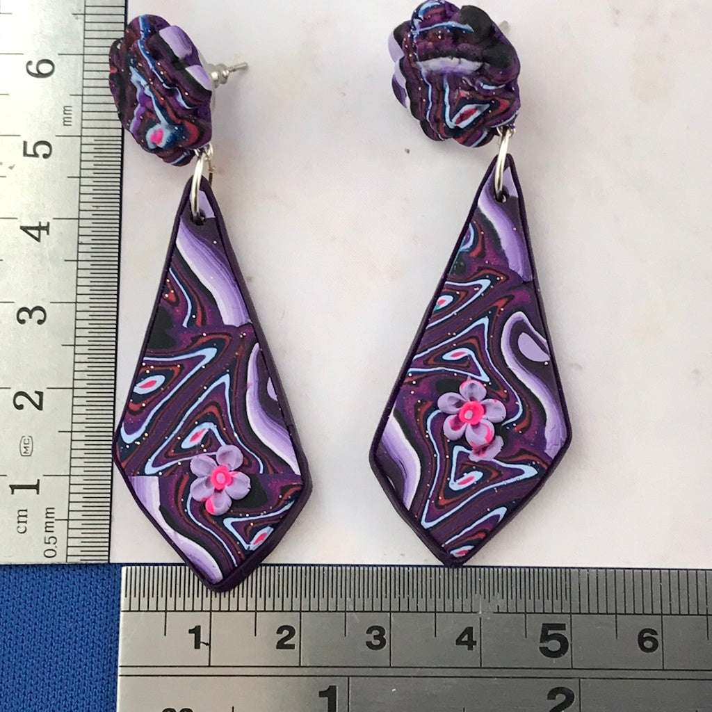 Rennique long groovy purple marbled polymer clay drop earrings with floral accent and size reference ruler.