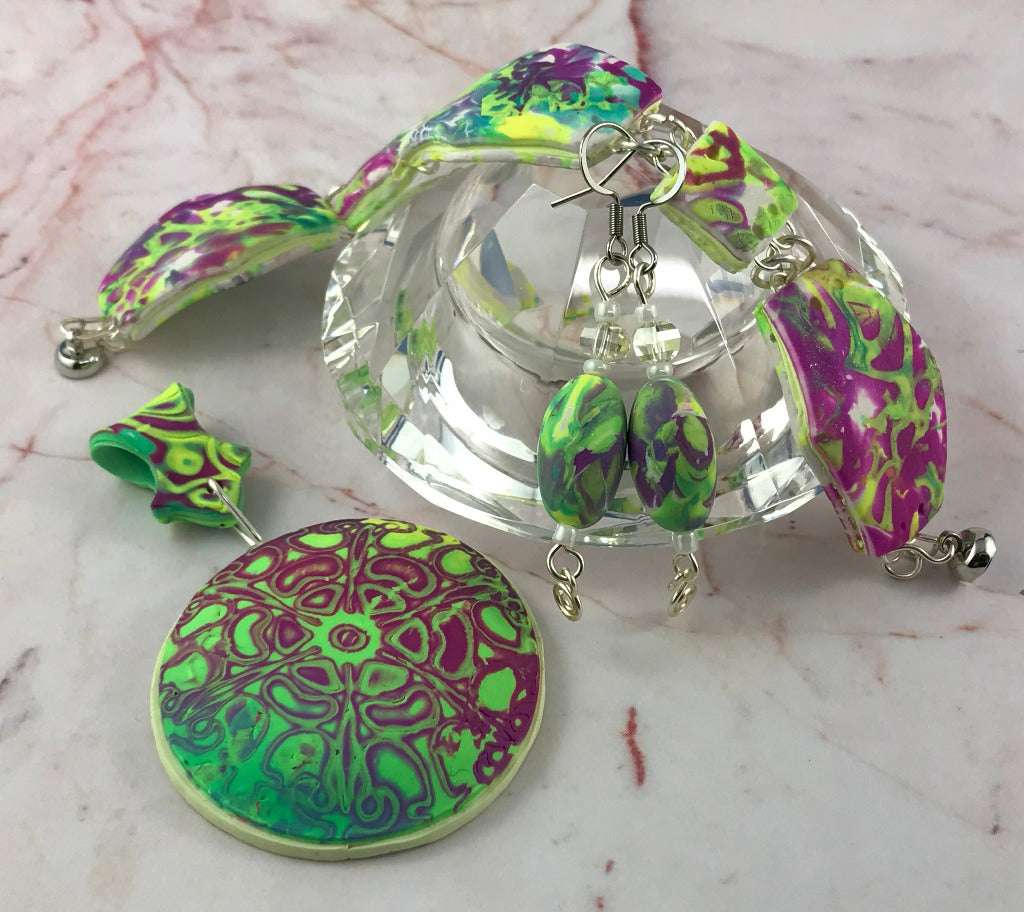 Flat lay of bold abstract handmade pendant, earrings, and bracelet jewellery set.