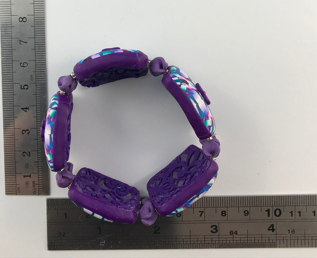 Handmade pink and purple stretch bracelet shown with ruler for size reference and measurement.