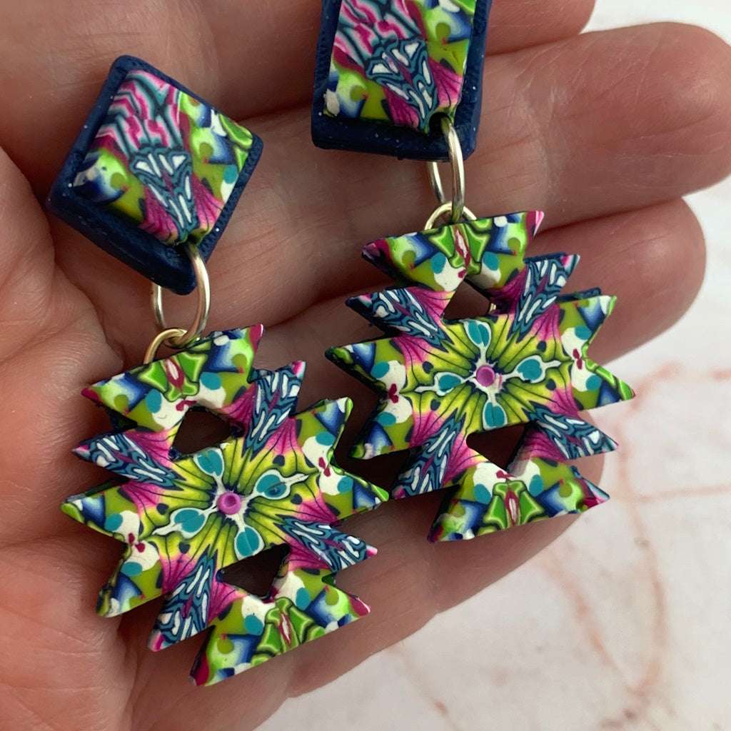 Close-up of colourful Australian handmade Aztec inspired statement earrings with bold pink green blue geometric pattern.