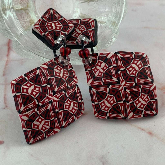 Styled product image of Australian artist made red diamond statement earrings with bold geometric red black and white pattern.