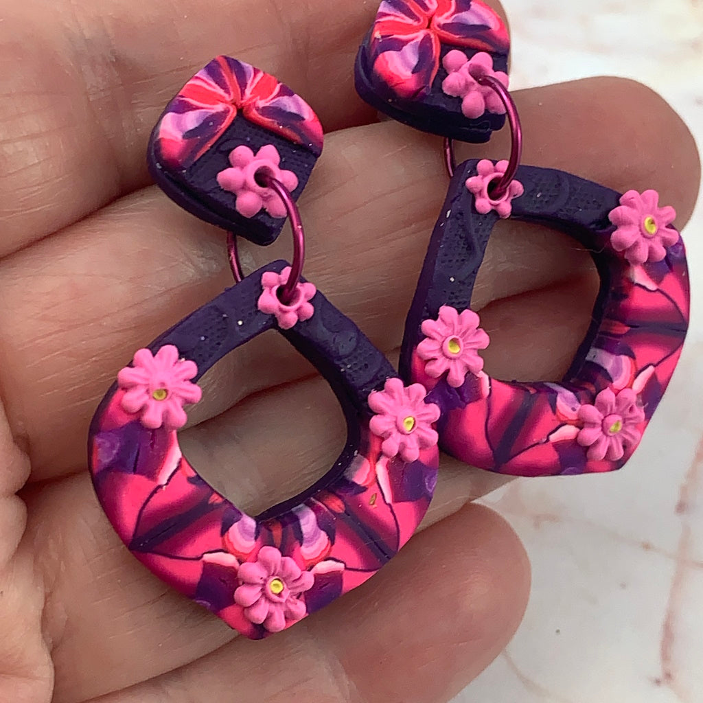 Angled close-up of award-winning Rennique hand-sculpted red diamond earrings with floral accents and bold pink marbled design.
