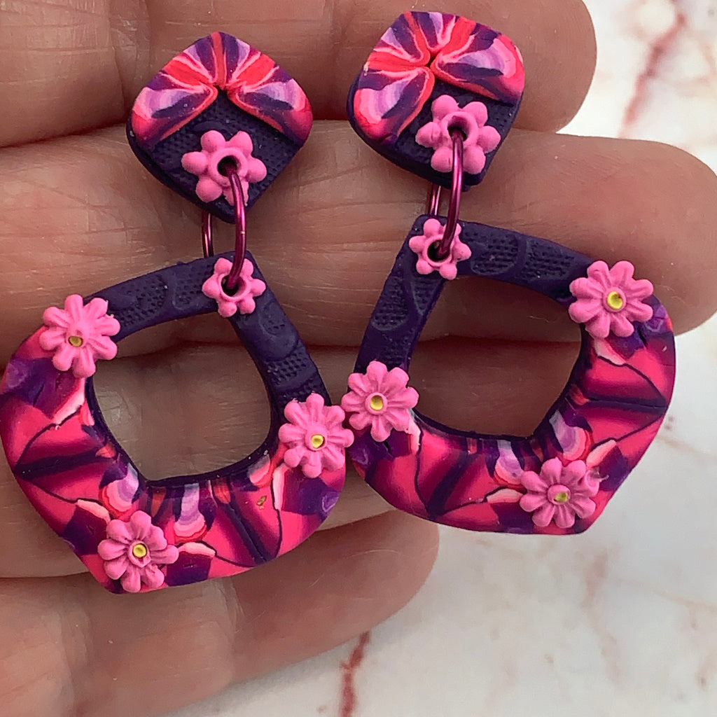 Close-up of award-winning Rennique hand-sculpted red diamond shape fashion earrings with pink flower embellishments and glossy finish.