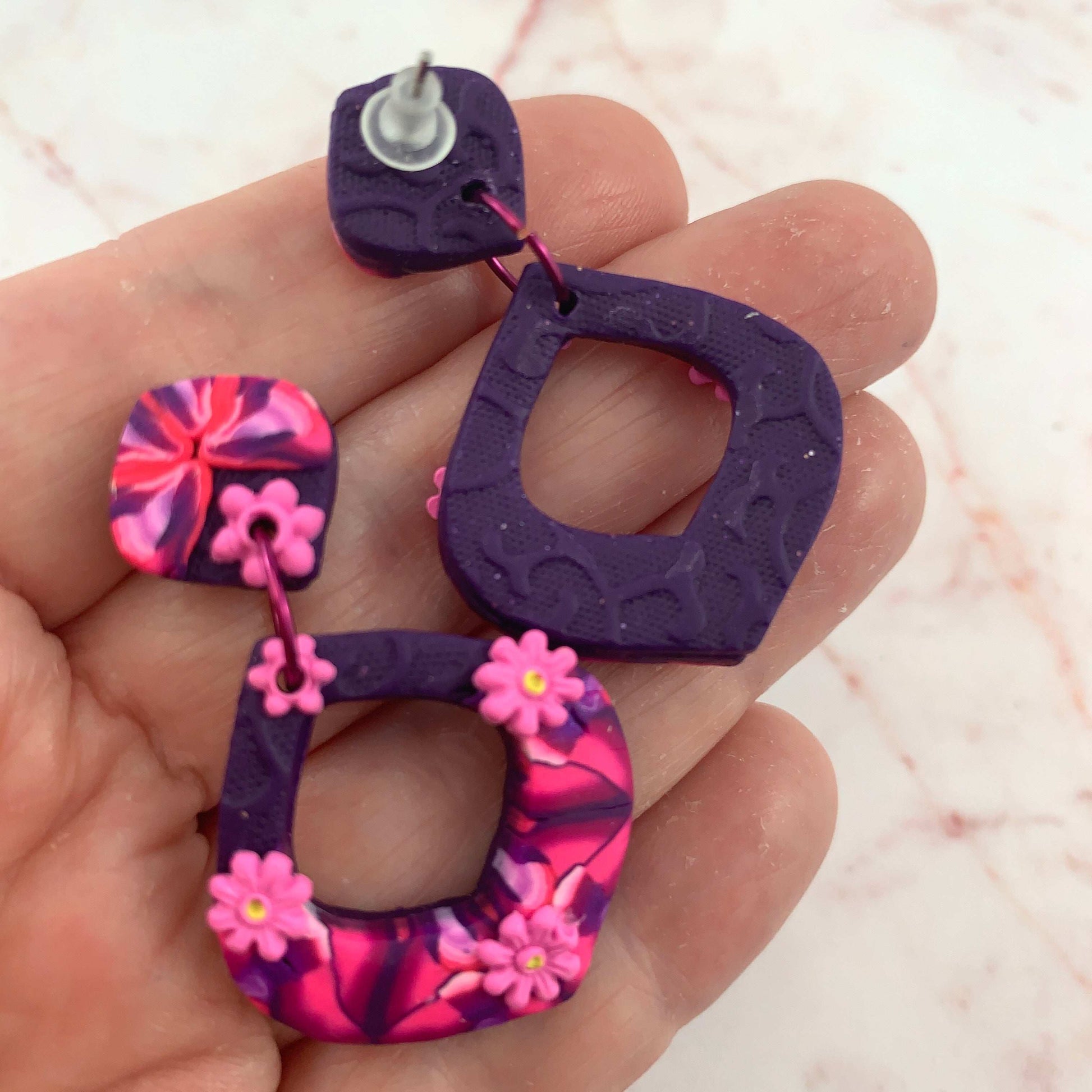 Award-winning Rennique hand-sculpted red diamond fashion earrings showing front floral design and textured back detail in hand.