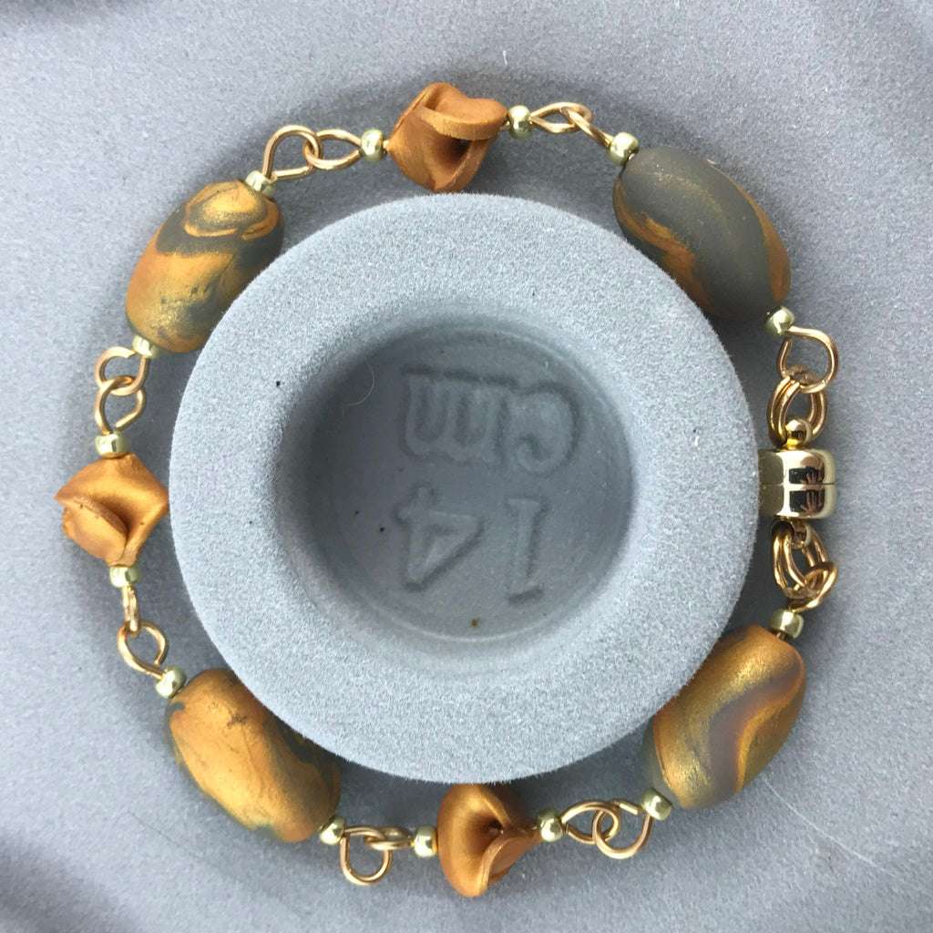 Handmade blue grey and gold bracelet shown on 14 cm size stand, featuring marbled oval beads and delicate floral accents.