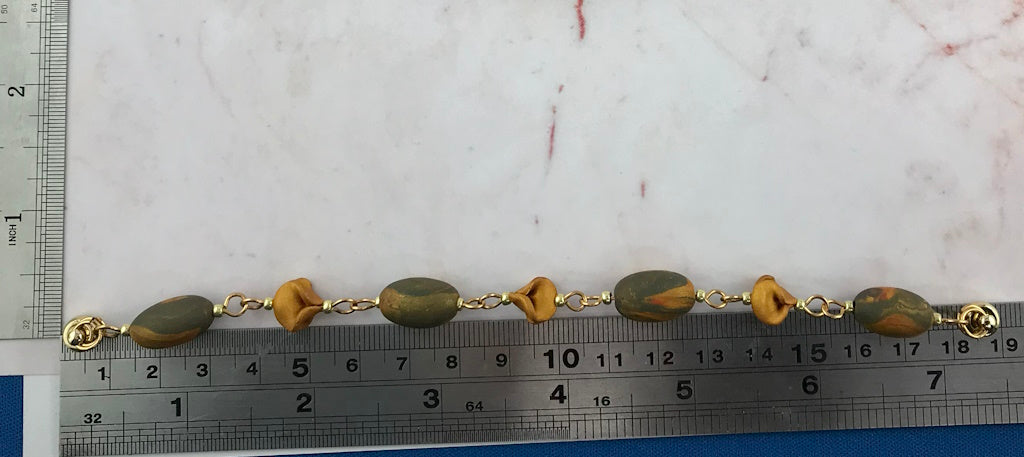 Handmade blue grey and gold bracelet laid flat with ruler, featuring oval beads and delicate floral accents in a matching leaf-inspired design.
