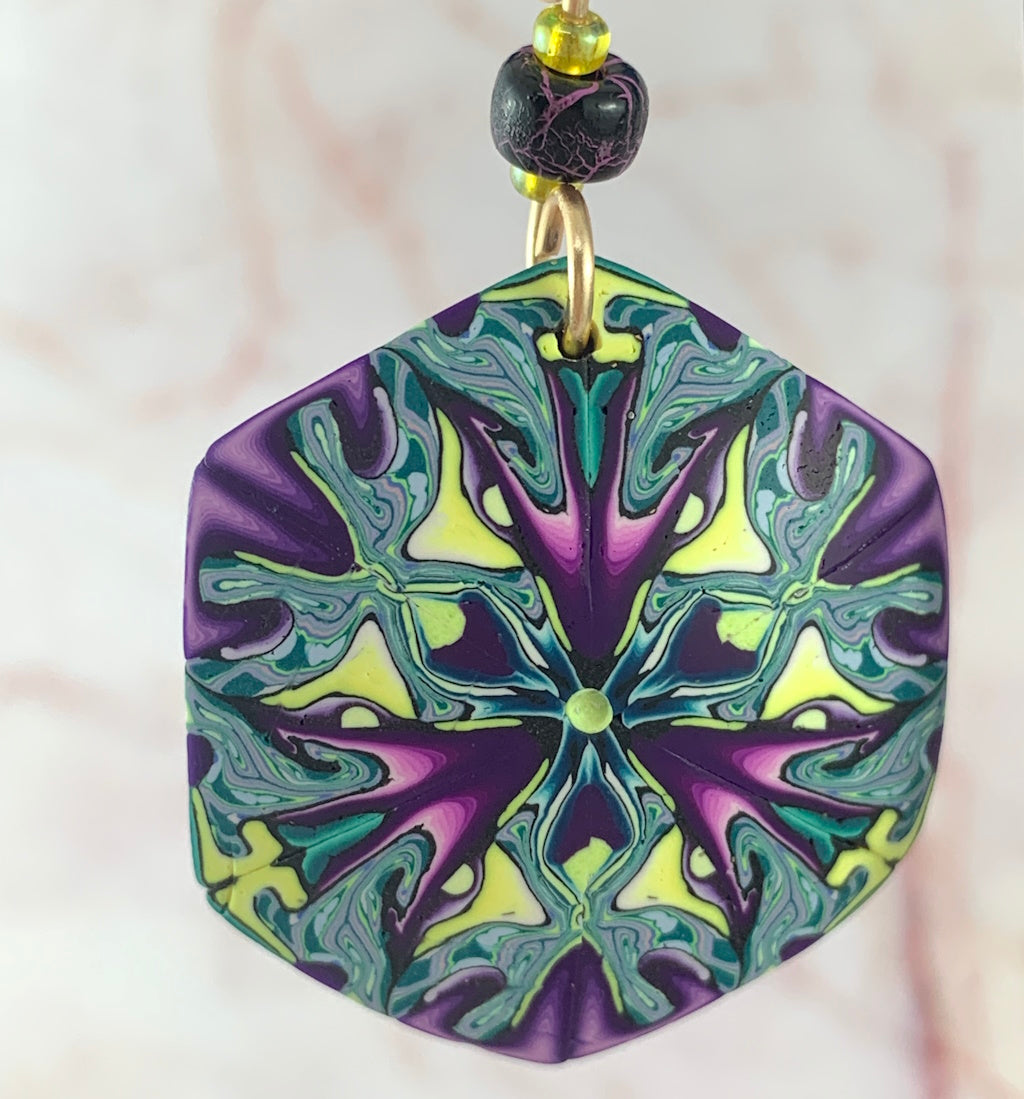 Close up of contemporary wearable art earrings with intricate geometric pattern in purple green and yellow tones