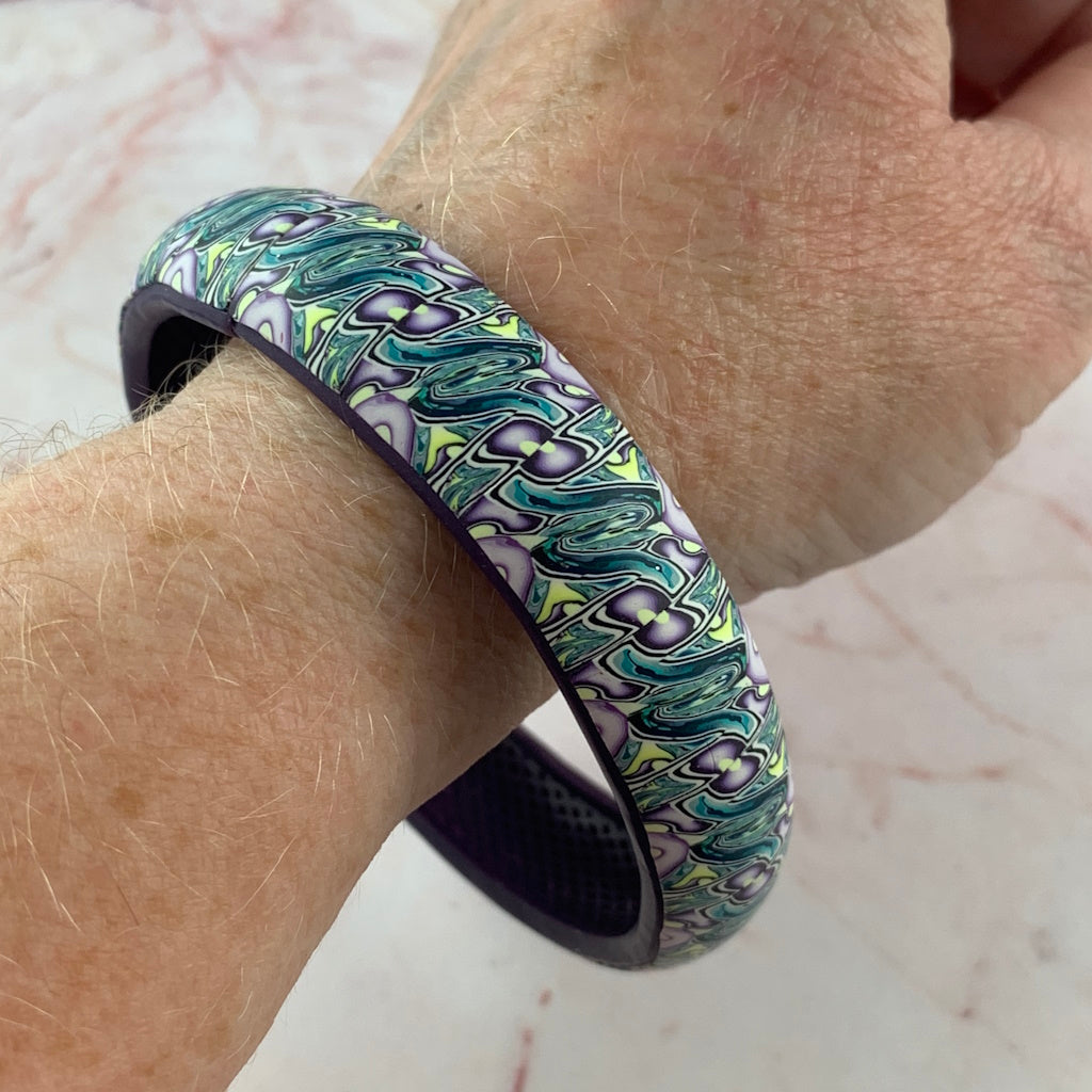 Designer polymer clay bangle by Rennique displayed on stand, handcrafted Australian statement bracelet with flowing pattern design