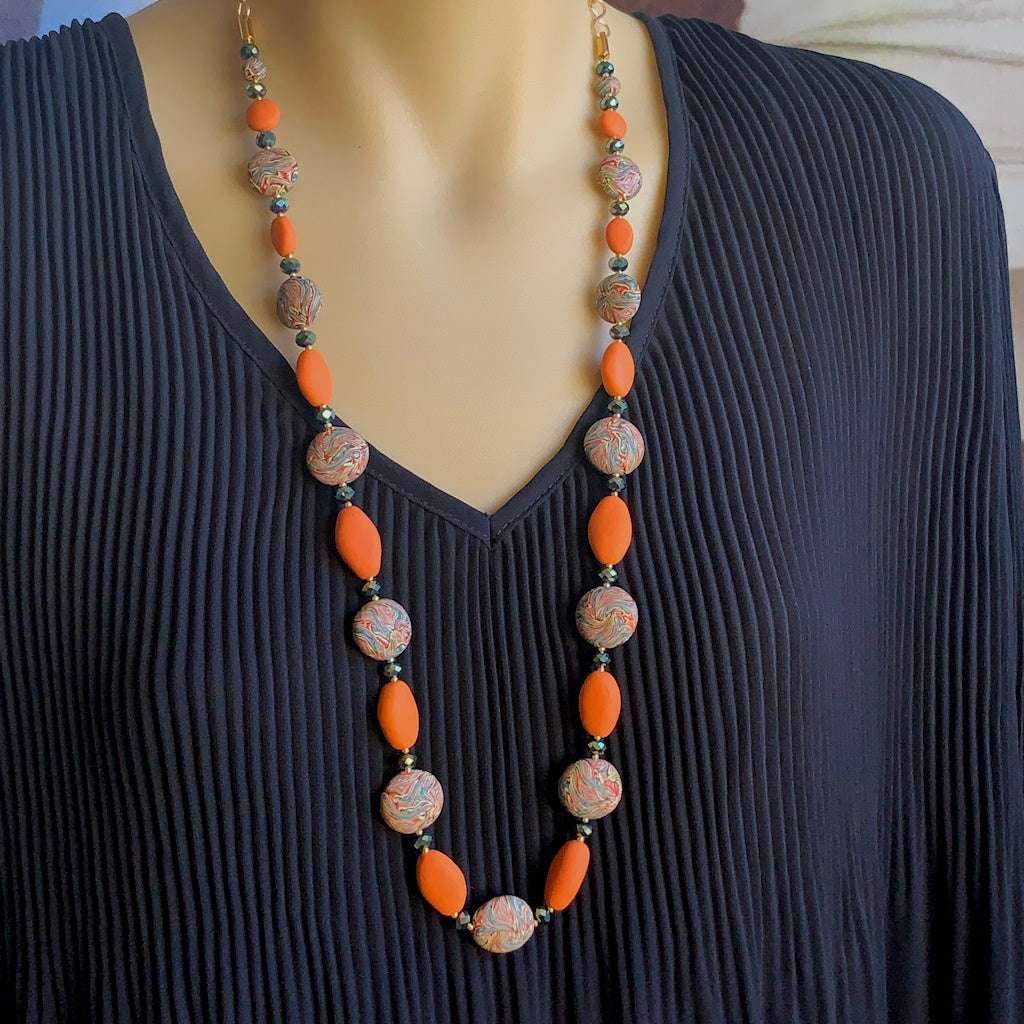 Flat lay of handmade long necklace with orange oval beads and marble patterned beads with matching earrings