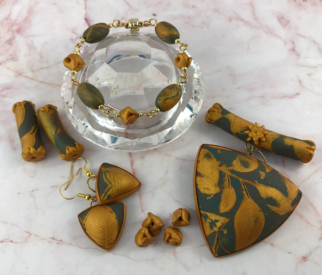 Blue and gold handmade jewellery set featuring lightweight leaf pendant, matching earrings and bracelet displayed on crystal stand.