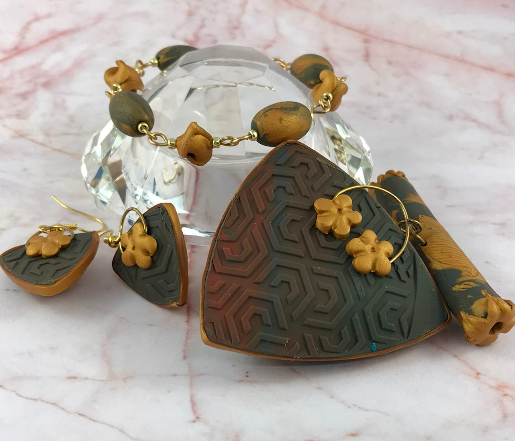 Blue and gold handmade jewellery set featuring lightweight leaf pendant, matching earrings and bracelet displayed on crystal stand.