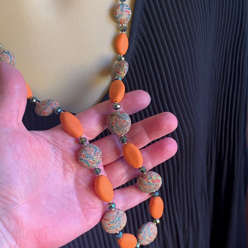 Hand holding long necklace with orange beads and patterned marble beads, handmade statement jewellery Australia