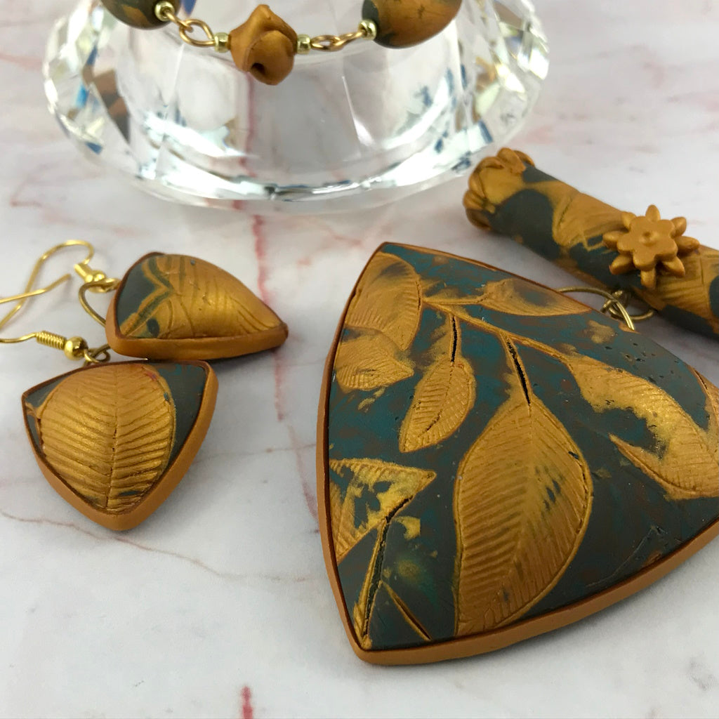 Elegant handmade polymer clay necklace and earrings set in soft blue grey and metallic gold with embossed leaf texture.