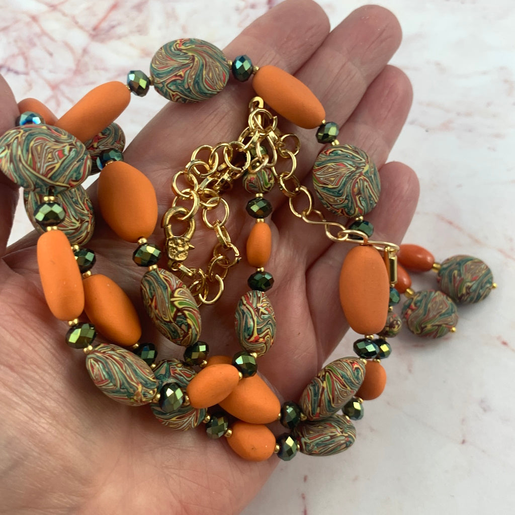 Close up of orange beads, green crystal spacers and marble patterned beads on handmade necklace