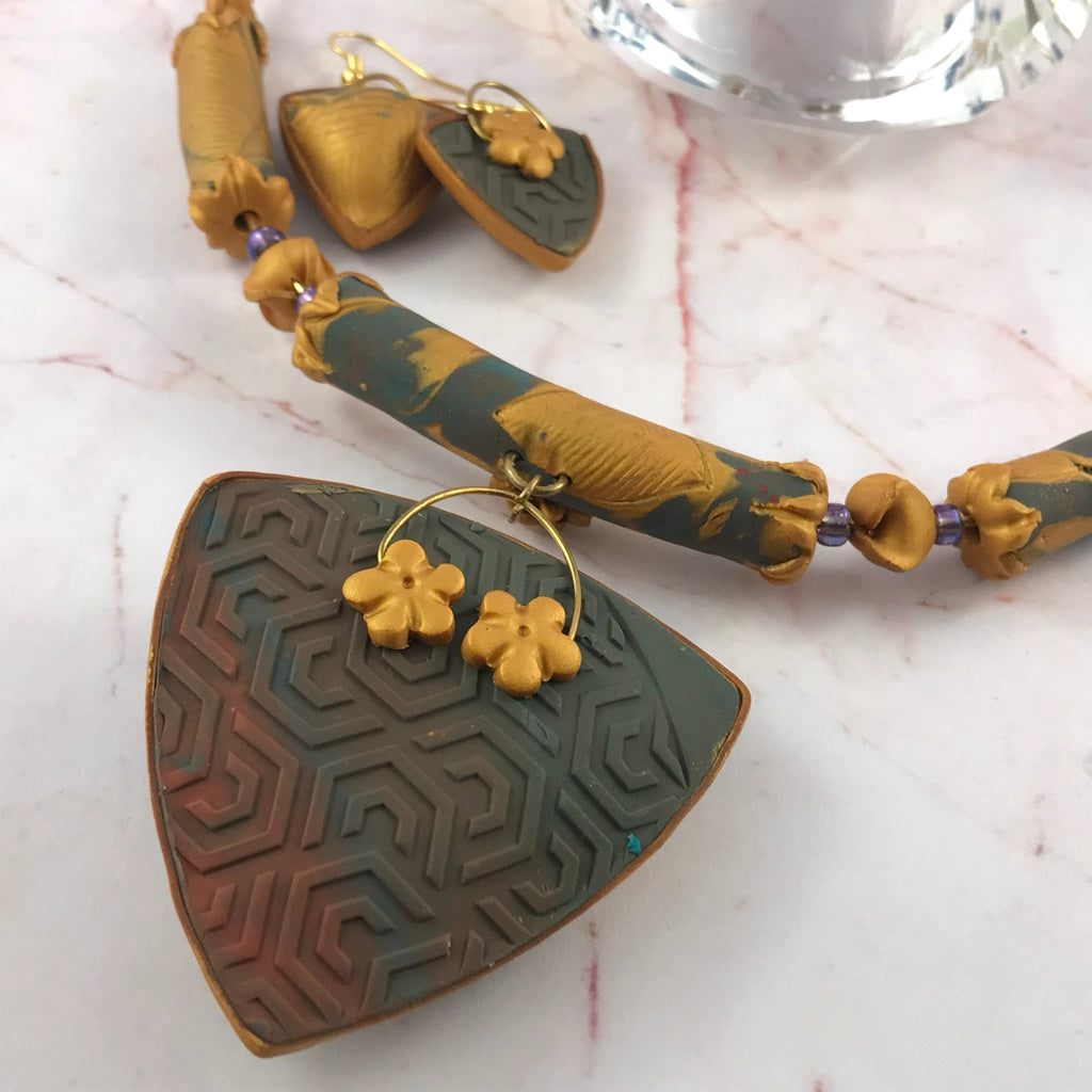Back view of handmade blue grey and gold polymer clay pendant necklace showing embossed geometric texture and matching floral bead collar.
