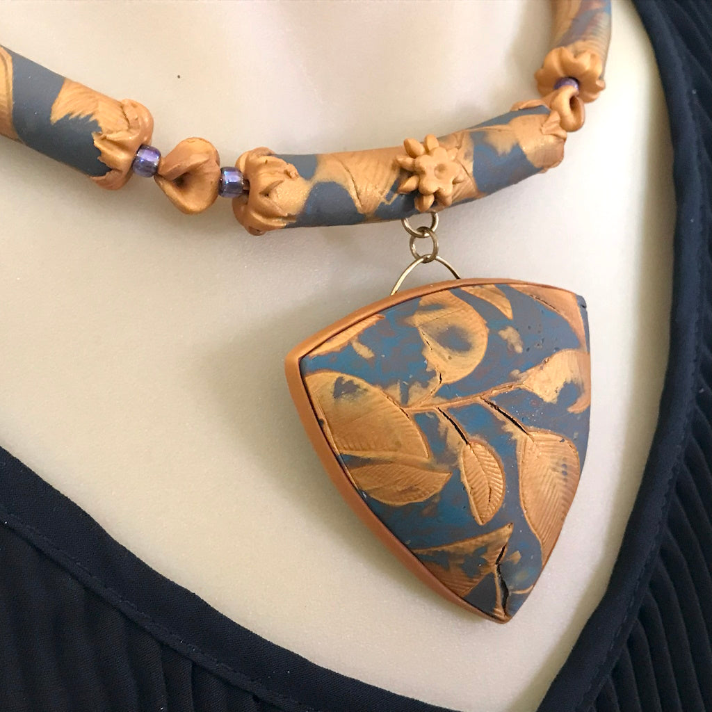 Blue and gold lightweight leaf pendant necklace worn on neckline, showing elegant embossed botanical pattern.