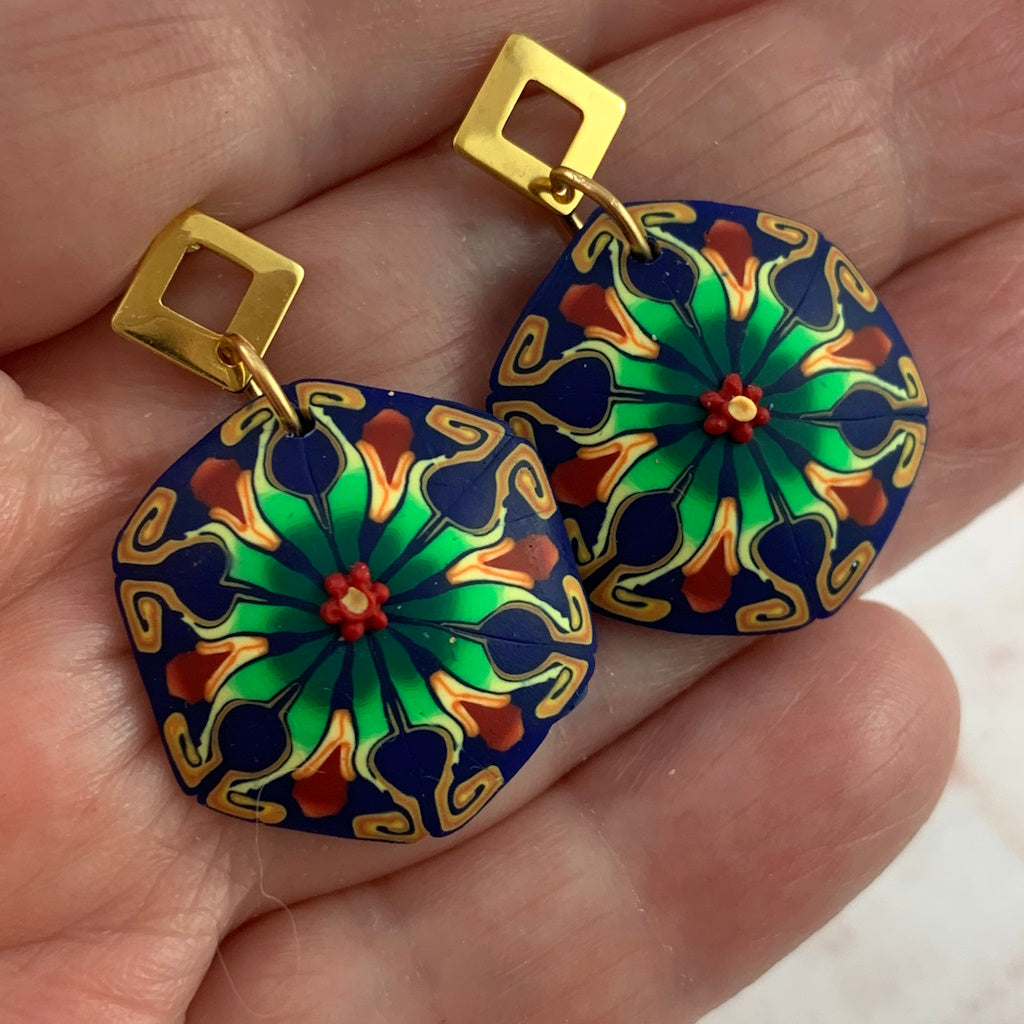 Close-up of handcrafted blue, green and gold floral statement earrings by Rennique in polymer clay.