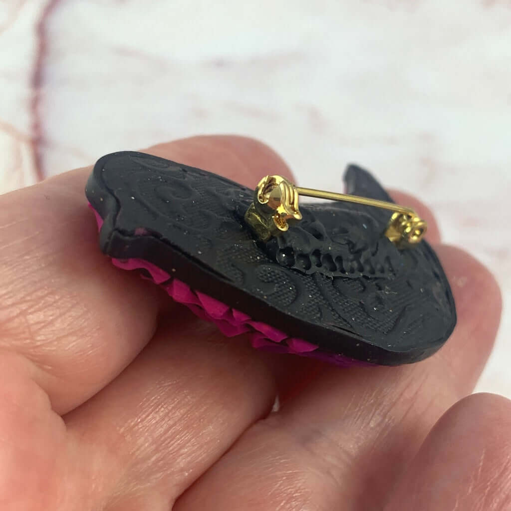 Side view of Rennique bird brooch showing thickness and layered polymer clay texture in pink and purple tones