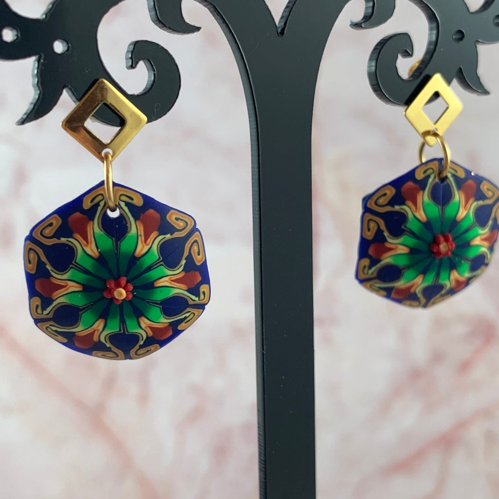 Blue and green tropical-inspired designer earrings by Rennique displayed on black jewellery stand with gold studs.