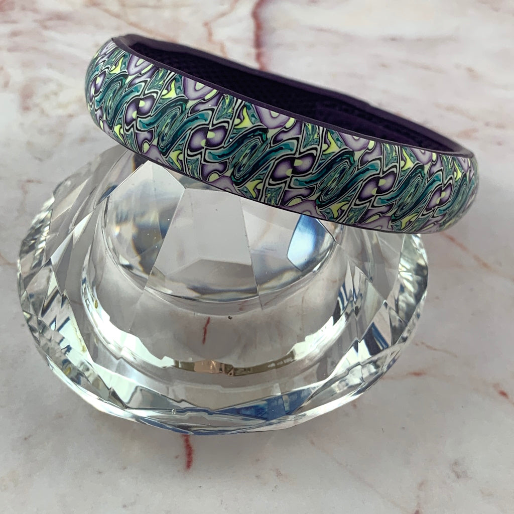 Rennique handmade statement bangle worn on wrist, featuring blue-green, lilac and pale yellow flowing pattern polymer clay bracelet
