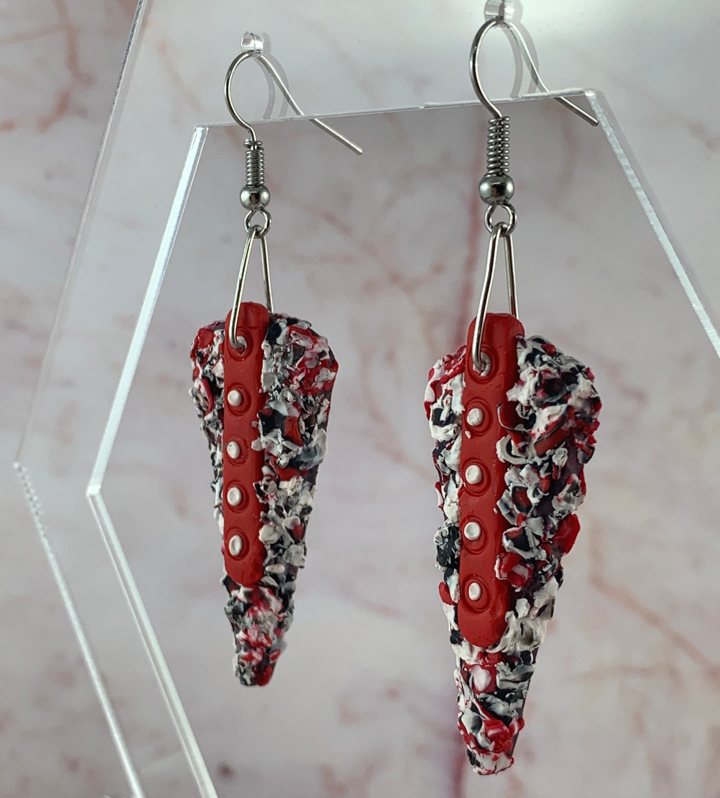 Rennique wearable art polymer clay earrings held in hand featuring textured red, black and white design