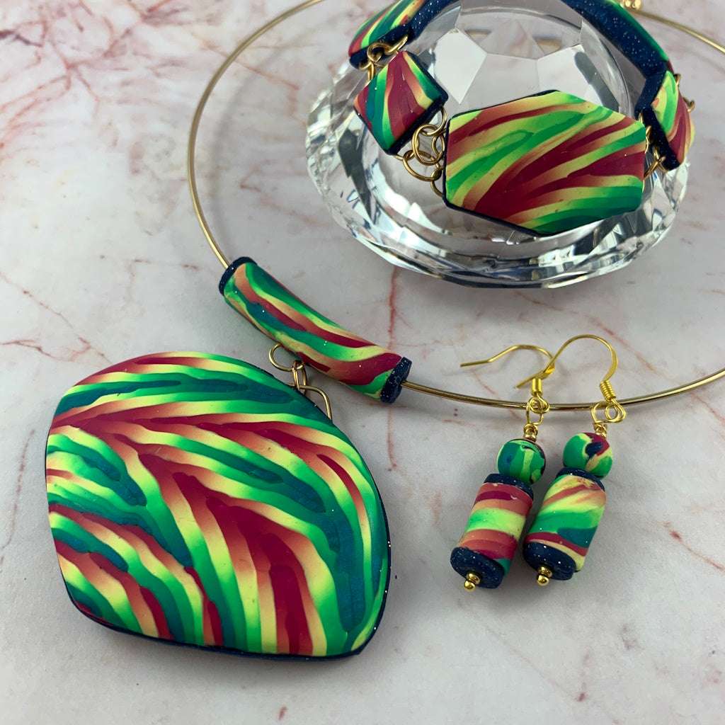 Close up of Rennique handmade artisan jewellery set with large statement pendant, matching drop earrings and bracelet in vibrant striped green, teal and pink polymer clay.