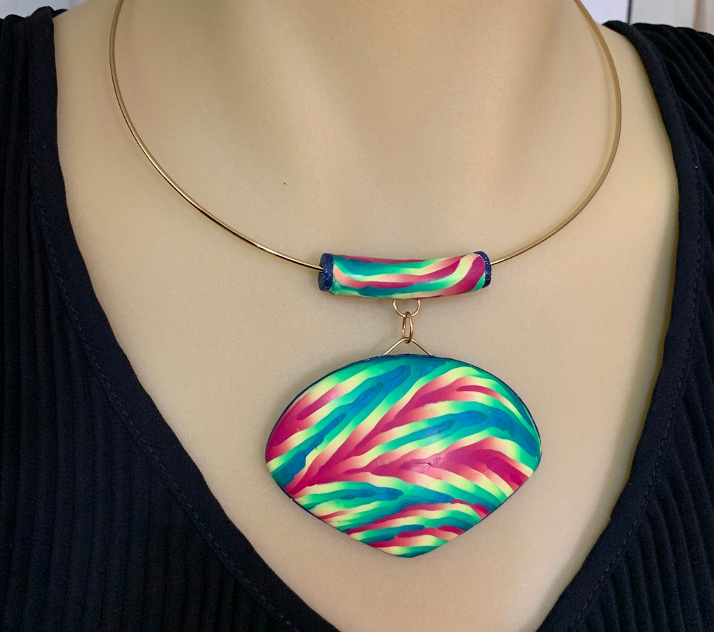 Rennique handmade colourful statement pendant necklace worn on display, featuring bold multicolour polymer clay pendant in green, pink and teal with gold collar wire.