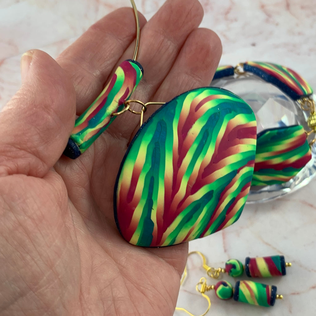Close up front view of Rennique large handmade statement pendant in vibrant green, teal and pink polymer clay with bold flowing striped design and gold hardware.