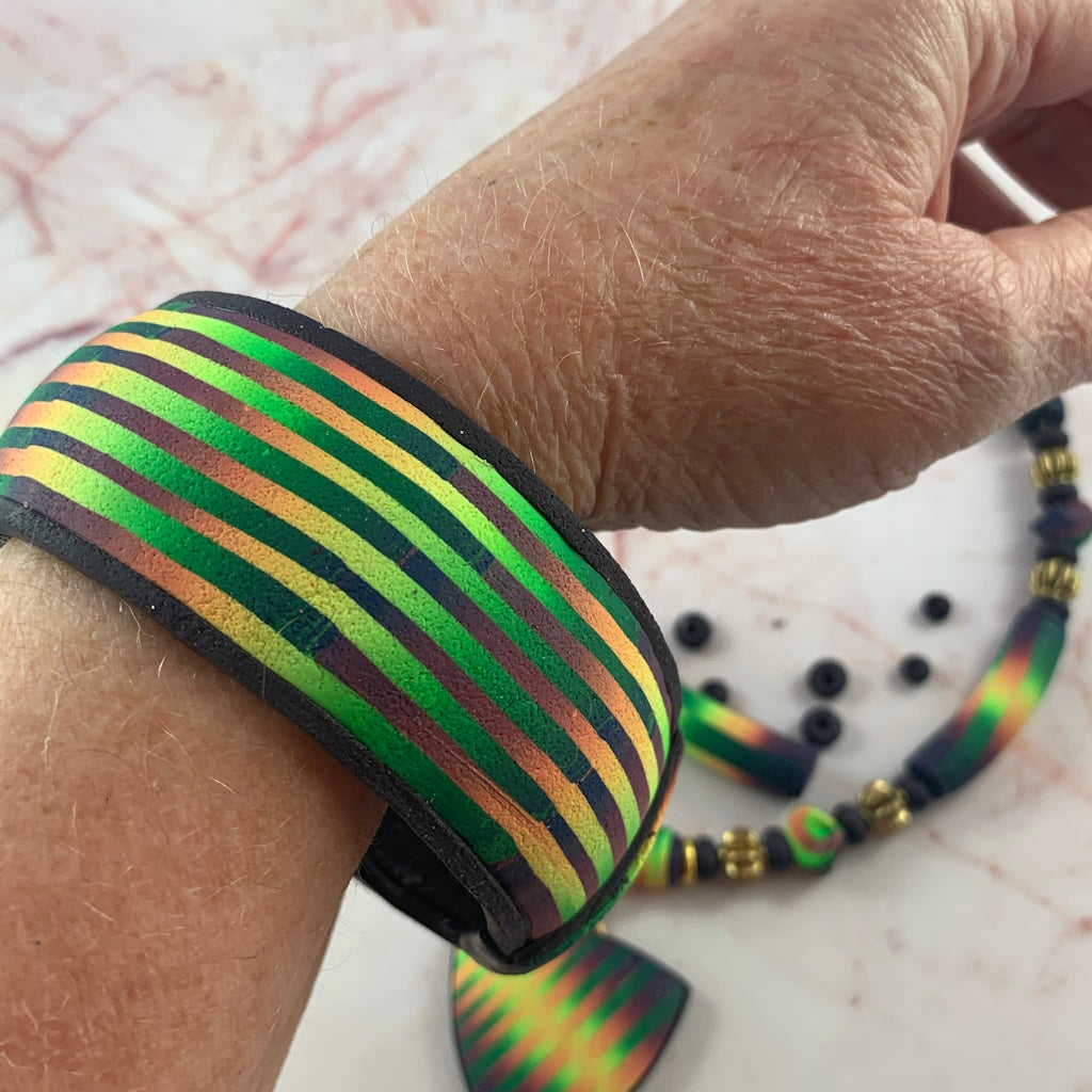 Award winning Rennique ladies statement bracelet with bold green gold purple striped artisan design worn on wrist.