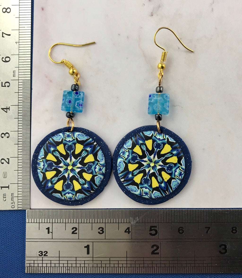 Handmade round blue and yellow earrings shown with ruler for size reference and scale.