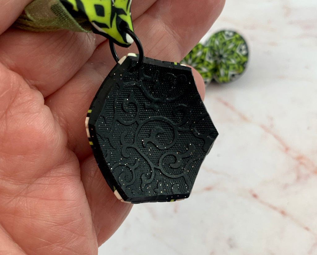 Back view of Rennique handcrafted polymer clay pendant with embossed black textured finish and subtle shimmer detail.