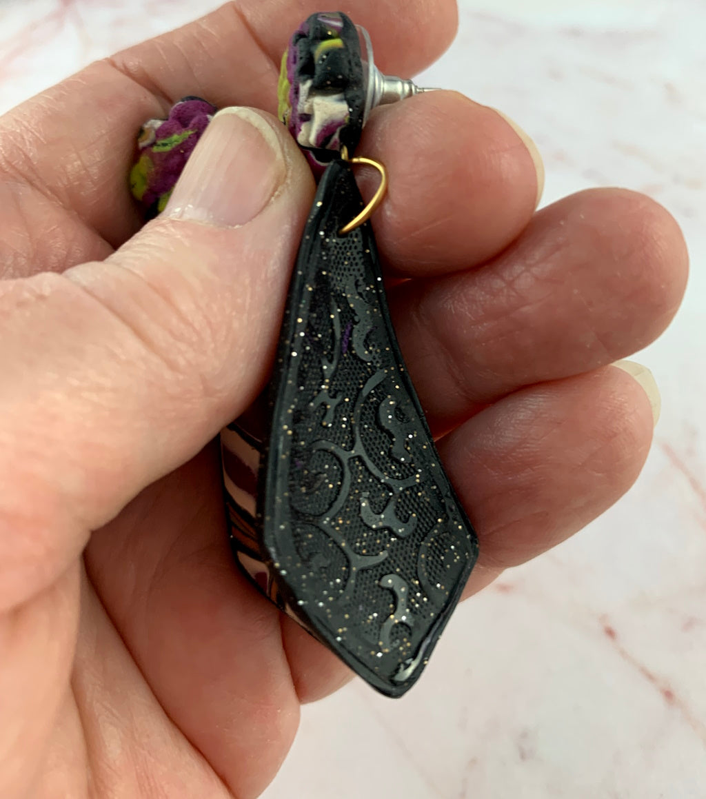 Macro close-up of handcrafted earrings showing textured polymer clay layers and sparkly finish.