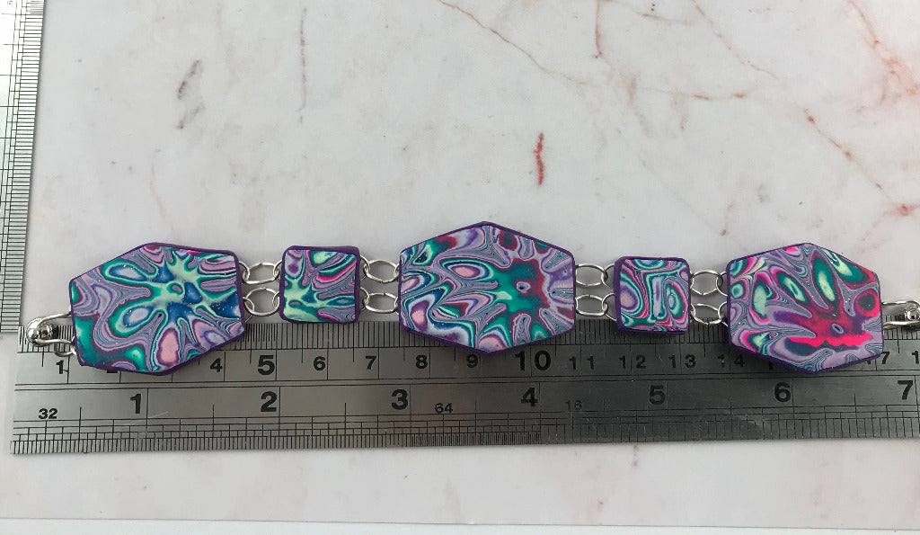 Flat lay view of geometric handmade bracelet in purple, teal and magenta marbled polymer clay, unique Australian artisan jewellery