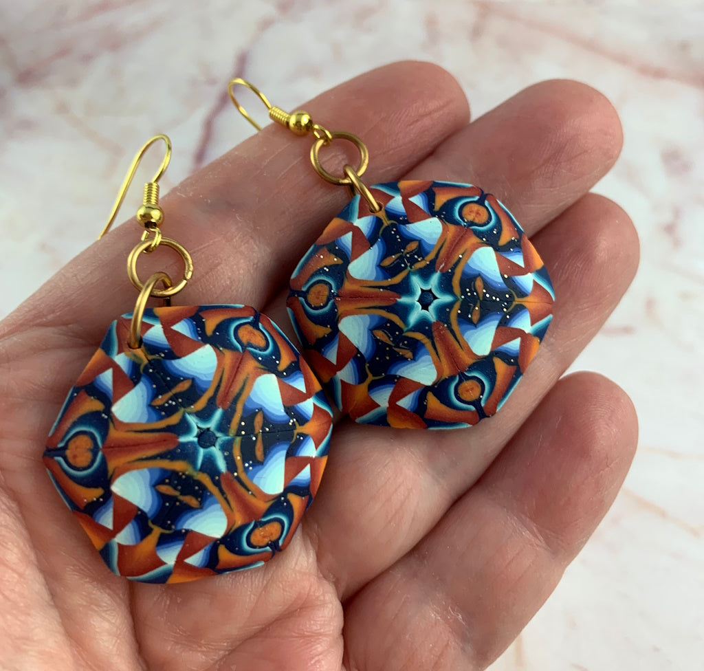Close-up of handmade artisan polymer clay drop earrings featuring intricate mandala-inspired geometric design in orange, teal blue and navy with gold findings.