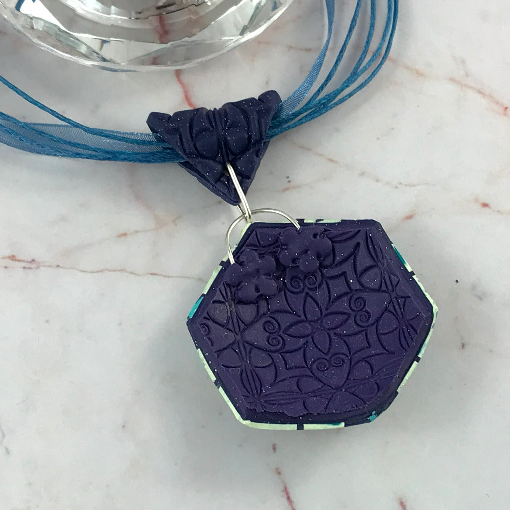 Back view of handmade artisan polymer clay pendant necklace showing textured floral embossed design