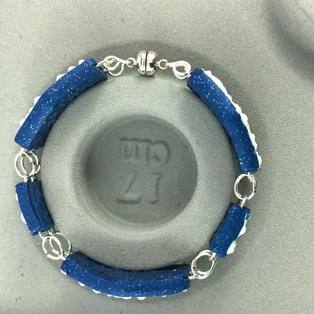 Blue and white artisan polymer clay bracelet displayed elegantly on crystal stand with silver connectors.