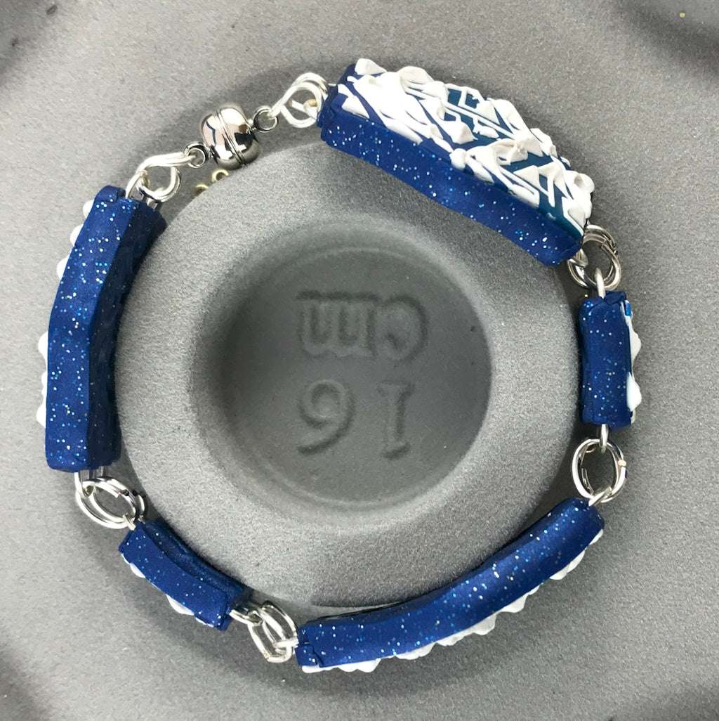 Handmade blue and white geometric polymer clay bracelet shown with 16 cm size reference, featuring silver link connectors and textured navy blue backing.