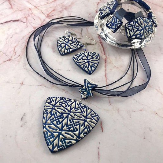 Handmade blue and white geometric polymer clay jewellery set featuring pendant necklace, earrings, and matching bracelet in flat lay display.