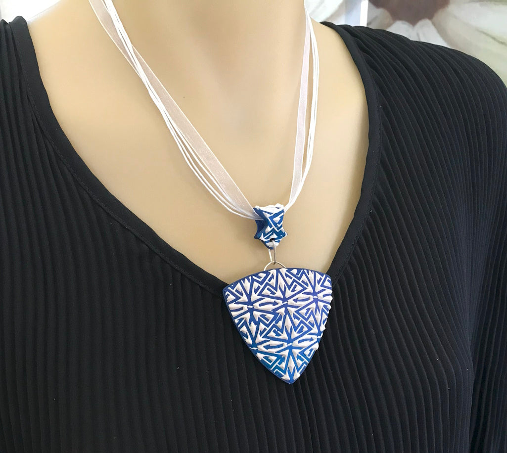 Front worn view of blue and white geometric pendant necklace styled on black outfit.
