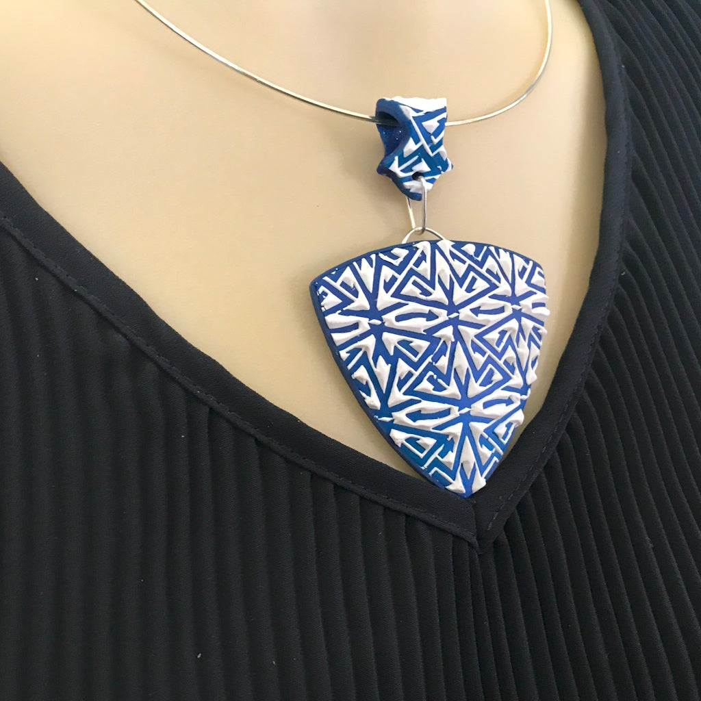 Blue and white geometric polymer clay statement pendant necklace worn on mannequin, showcasing bold artisan design.