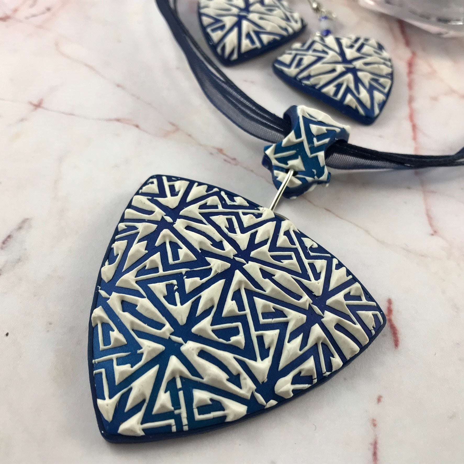 Close-up of handmade blue and white geometric polymer clay triangle pendant with raised textured pattern.