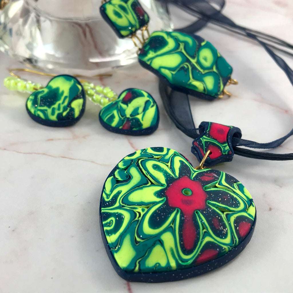 Handmade Colour Burst Flower jewellery set flat lay with heart pendant, bracelet and matching earrings in bold floral polymer clay design