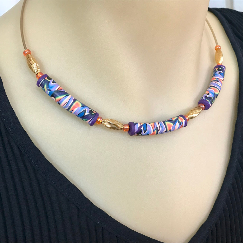 Handmade colourful statement necklace worn, featuring marbled polymer clay beads and gold accent details.