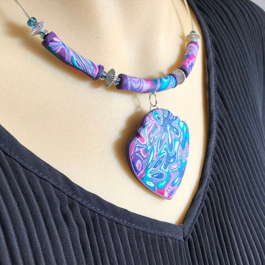 Handmade Cosmic Flower heart pendant necklace worn on model featuring bold purple, teal and pink artisan polymer clay design
