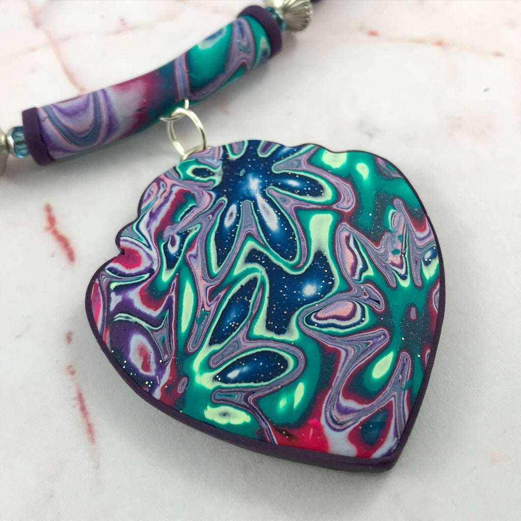 Close-up of handmade heart pendant necklace in purple, teal and pink marbled polymer clay with cosmic floral swirl design, artisan jewellery Australia