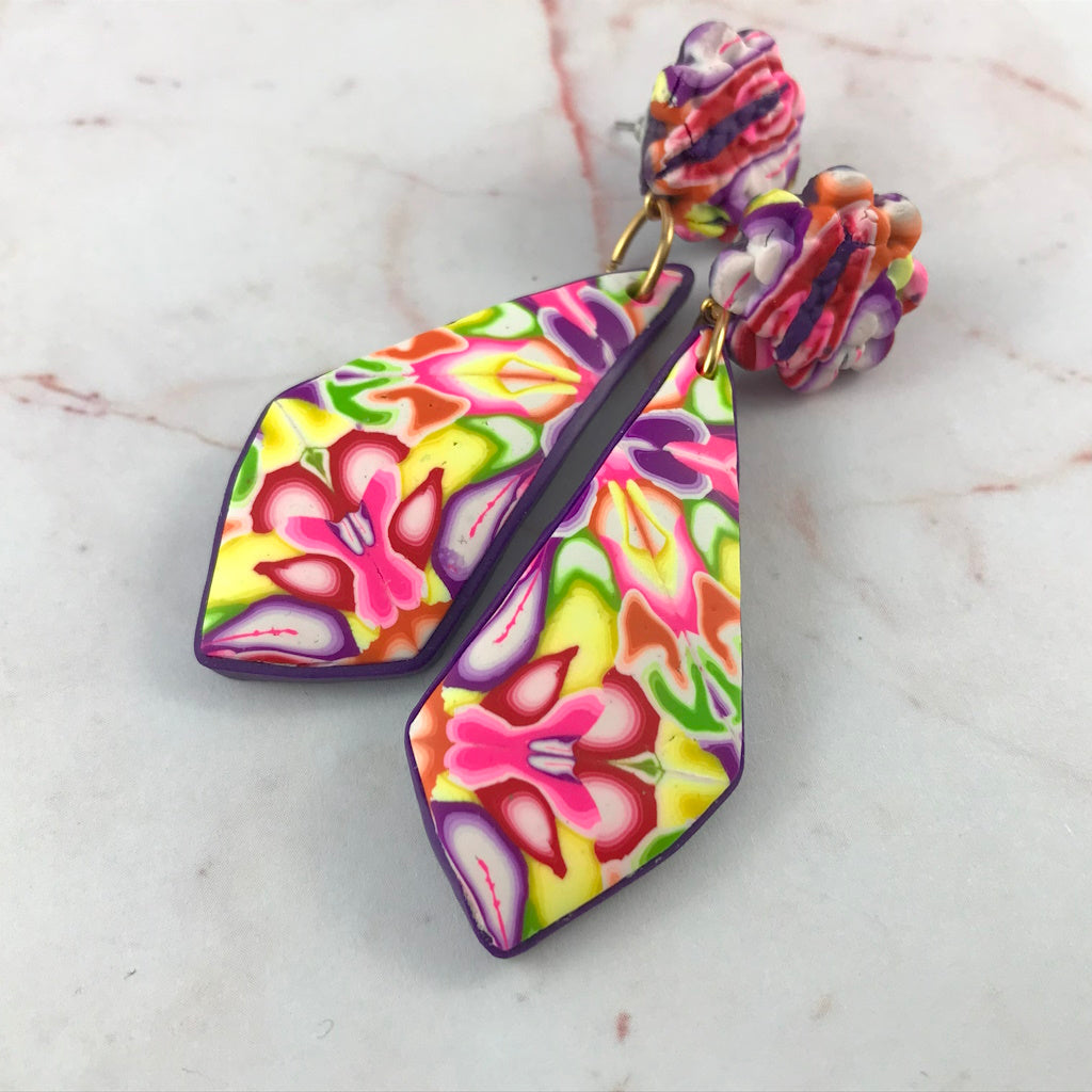 Close-up of handmade floral polymer clay drop earrings in pink, lime, purple, and white by Rennique Australia.