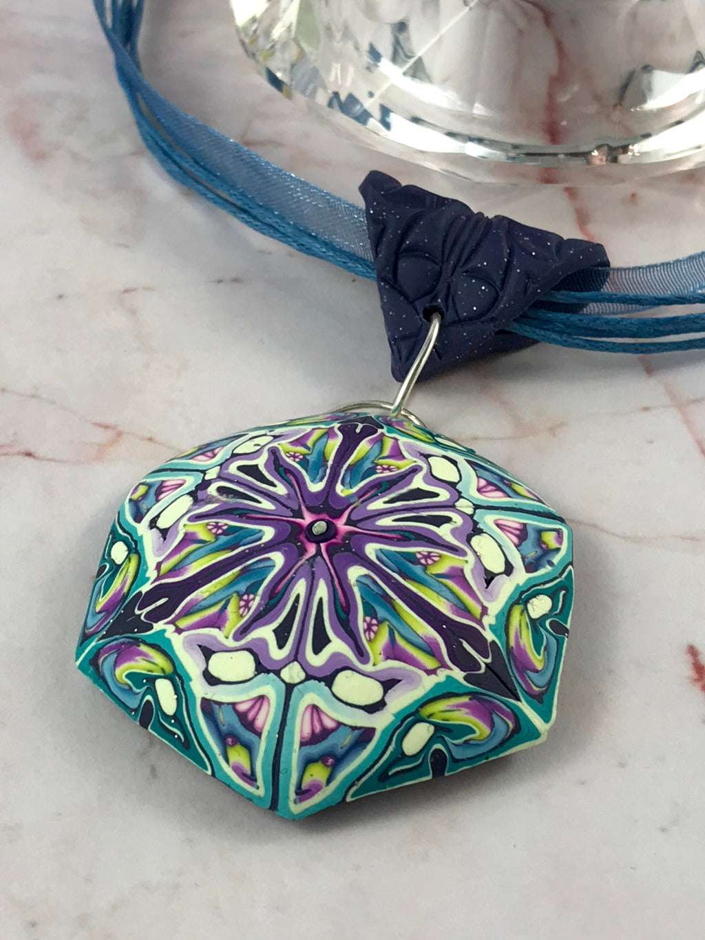 Front view of handmade passionfruit flower inspired polymer clay pendant necklace in pastel blue, purple and lilac tones