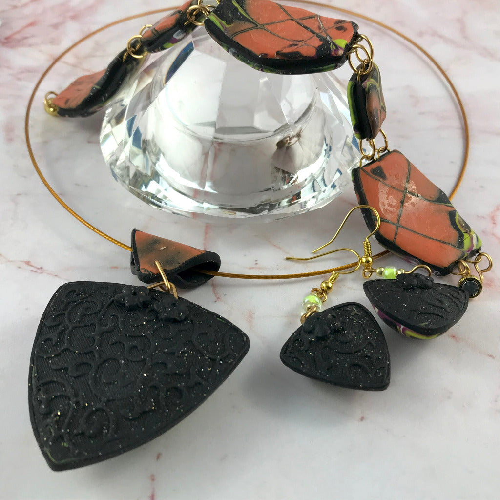 Handmade polymer clay bracelet with magnetic clasp, bold abstract pattern in orange green black tones, lightweight curved pieces on crystal display, artisan jewellery Australia