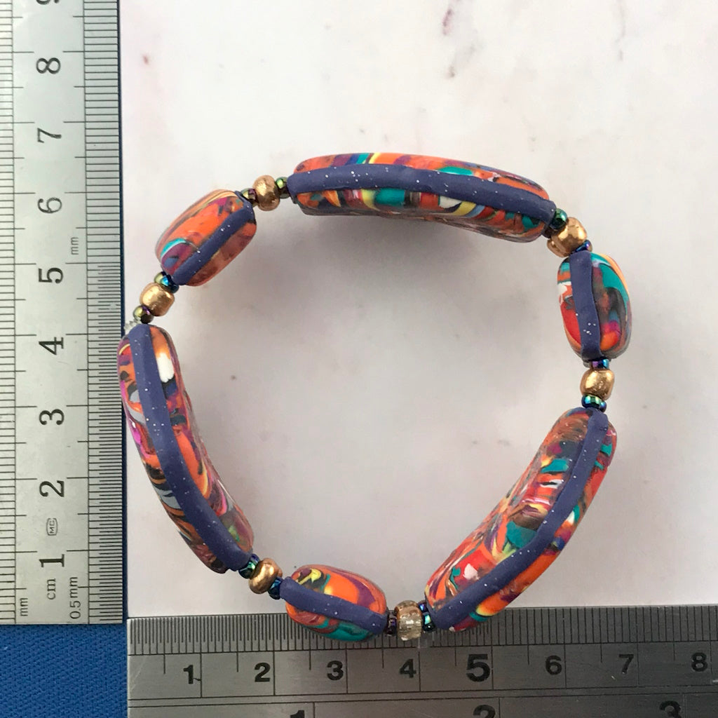 Handmade multicolor polymer clay bracelet shown with ruler for size reference, featuring abstract swirl design in orange, teal, magenta, and navy.